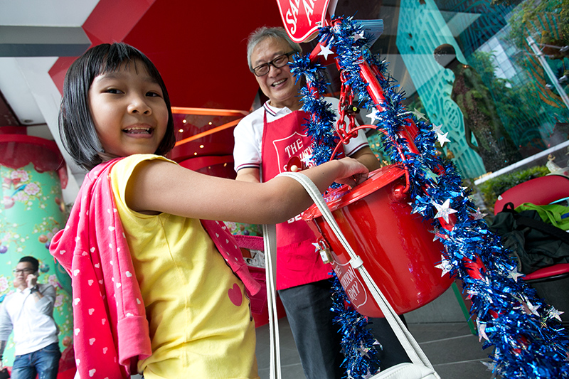 A young girl putting money into The Salvation Army Christmas Kettling bucket.